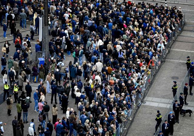 Spectators arrive next to police officers at Dam Square prior to the National Remembrance Day ceremony on Dam Square in Amsterdam on May 4, 2026. During Remembrance Day, the victims of the Second World War in Europe and Southeast Asia are commemorated, as well as the victims of subsequent war situations and peacekeeping operations in which the Netherlands was involved. (Photo by Patrick van Emst / POOL / AFP) / Netherlands OUT