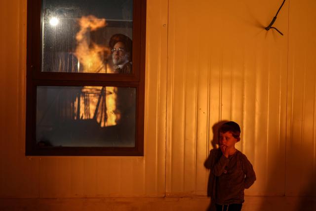 A bonfire is reflected on a window as a man and young boy look on while ultra-Orthodox Jews celebrate Lag BaOmer in Jerusalem on May 4, 2026. Lag BaOmer marks the anniversary of the death of Talmudic sage Rabbi Shimon Bar Yochai approximately 1,900 years ago. (Photo by Ilia YEFIMOVICH / AFP)