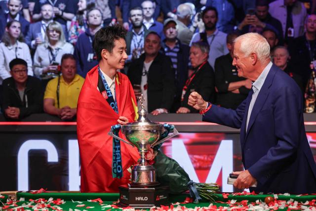 China's Wu Yize (L) is congratulated by English sporting promotor Harry Hearn (R) during the awards ceremony after his victory over England's Shaun Murphy in the World Snooker Championship final round at The Crucible in Sheffield, northern England on May 4, 2026. (Photo by Darren Staples / AFP)