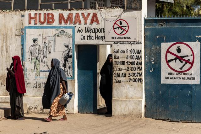Residents and patients walk past a “no weapons allowed” sign at the entrance of a public hospital in Kismayo, on April 22, 2026. Millions of people in Somalia are facing the repercussions of a severe drought after three consecutive failed raining seasons. Kismayo, the capital of Jubaland State in southern Somalia, is one of the largest IDP-receiving cities in the Horn of Africa country, receiving hundreds of thousands of people fleeing the prolonged drought and conflict. Save the Children provides health and nutrition services in the region. (Photo by SIMON MAINA / AFP)