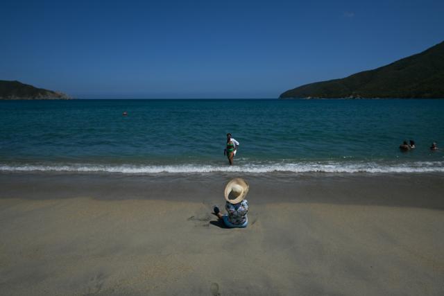 Tourists are seen at Bahia Concha in Tayrona National Natural Park, Magdalena Department, on April 16, 2026. At first glance, it appears to be a postcard-perfect tourist jewel, with crystal-clear Caribbean waters and mountains crowned by snowcapped peaks. But beneath the surface of Colombias idyllic destination, paramilitary violence keeps shopkeepers and Indigenous communities living in fear. In the Sierra Nevada de Santa Marta, tourists roam unaware of camouflaged squads monitoring them from close range, extorting nearby businesses and spreading terror among Indigenous communities, whose ancestral knowledge has been recognized by UNESCO as part of the worlds cultural heritage. (Photo by Luis ACOSTA / AFP)