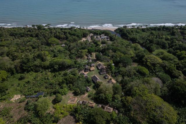 Aerial view of the Kutunsama Indigenous Reservation in Tayrona National Natural Park, Magdalena department, Colombia, on April 18, 2026. At first glance, it appears to be a postcard-perfect tourist jewel, with crystal-clear Caribbean waters and mountains crowned by snowcapped peaks. But beneath the surface of Colombias idyllic destination, paramilitary violence keeps shopkeepers and Indigenous communities living in fear. In the Sierra Nevada de Santa Marta, tourists roam unaware of camouflaged squads monitoring them from close range, extorting nearby businesses and spreading terror among Indigenous communities, whose ancestral knowledge has been recognized by UNESCO as part of the worlds cultural heritage. (Photo by Luis ACOSTA / AFP)