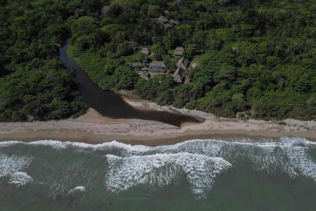 Aerial view of the Kutunsama Indigenous Reservation in Tayrona National Natural Park, Magdalena department, Colombia, on April 18, 2026. At first glance, it appears to be a postcard-perfect tourist jewel, with crystal-clear Caribbean waters and mountains crowned by snowcapped peaks. But beneath the surface of Colombias idyllic destination, paramilitary violence keeps shopkeepers and Indigenous communities living in fear. In the Sierra Nevada de Santa Marta, tourists roam unaware of camouflaged squads monitoring them from close range, extorting nearby businesses and spreading terror among Indigenous communities, whose ancestral knowledge has been recognized by UNESCO as part of the worlds cultural heritage. (Photo by Luis ACOSTA / AFP)