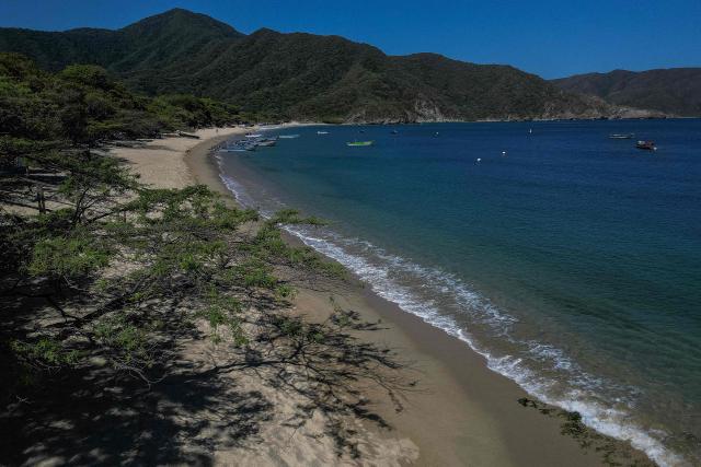 Aerial view of Bahia Concha in Tayrona National Natural Park, Magdalena department, Colombia, on April 16, 2026. At first glance, it appears to be a postcard-perfect tourist jewel, with crystal-clear Caribbean waters and mountains crowned by snowcapped peaks. But beneath the surface of Colombias idyllic destination, paramilitary violence keeps shopkeepers and Indigenous communities living in fear. In the Sierra Nevada de Santa Marta, tourists roam unaware of camouflaged squads monitoring them from close range, extorting nearby businesses and spreading terror among Indigenous communities, whose ancestral knowledge has been recognized by UNESCO as part of the worlds cultural heritage. (Photo by Luis ACOSTA / AFP)