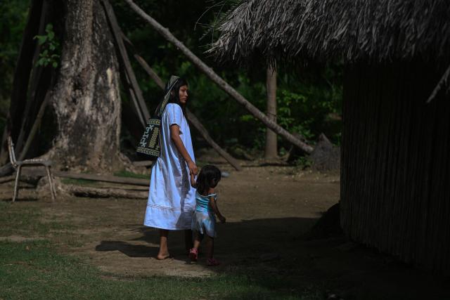 An Arhuaco Indigenous woman walks with her child at the Kutunsama Indigenous Reservation in Tayrona National Natural Park, Magdalena department, Colombia, on April 18, 2026. At first glance, it appears to be a postcard-perfect tourist jewel, with crystal-clear Caribbean waters and mountains crowned by snowcapped peaks. But beneath the surface of Colombias idyllic destination, paramilitary violence keeps shopkeepers and Indigenous communities living in fear. In the Sierra Nevada de Santa Marta, tourists roam unaware of camouflaged squads monitoring them from close range, extorting nearby businesses and spreading terror among Indigenous communities, whose ancestral knowledge has been recognized by UNESCO as part of the worlds cultural heritage. (Photo by Luis ACOSTA / AFP)