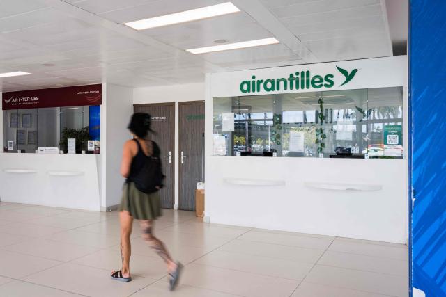 This photograph taken in Les Abymes, on the French Caribbean island of Guadeloupe on April 30, 2026, shows a passenger walking past a closed office of French regional airline Air Antilles at Maryse Conde airport's regional terminal. The regional airline, which had been serving the French Caribbean islands (Saint Barthélemy, Saint Martin, Guadeloupe and Martinique) since 2002, had been facing a series of setbacks for several years. On April 27, 2026, the Commercial Court of Pointe-à-Pitre (Guadeloupe) placed Air Antilles into administration, due to the lack of a takeover bid deemed credible. (Photo by Carla Bernhardt / AFP)