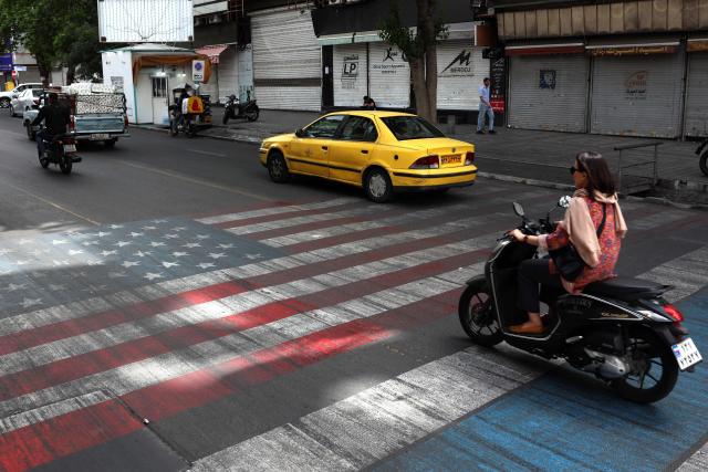 An Iranian woman rides his moped across a painted depiction of the Israeli flag and US flag on a street in the south of Tehran on May 5, 2026. The United Kingdom, France, Germany and Saudi Arabia called  for de-escalation in the Middle East following reported attacks on May 4, on the United Arab Emirates. (Photo by AFP) / 