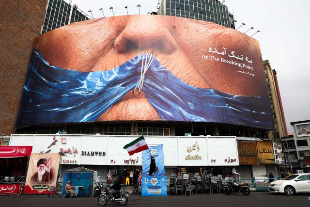 A woman waves an Iranian flag in front of an anti-US billboard referring to US President Donald Trump and the Strait of Hormuz at Valiasr Square in Tehran on May 5, 2026. Iran's chief negotiator in talks with the United States warned on May 5 that his country has "not even started" in its standoff over the Strait of Hormuz. (Photo by AFP) / 