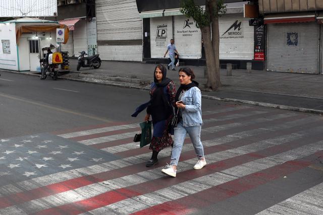 Iranians walk across a painted depiction of the US flag on a street in the south of Tehran on May 5, 2026. The United Kingdom, France, Germany and Saudi Arabia called  for de-escalation in the Middle East following reported attacks on May 4, on the United Arab Emirates. (Photo by AFP) / 
