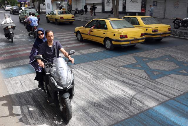 Iranians drive their vehicles across a painted depiction of the Israeli flag and US flag on a street in the south of Tehran on May 5, 2026. The United Kingdom, France, Germany and Saudi Arabia called  for de-escalation in the Middle East following reported attacks on May 4, on the United Arab Emirates. (Photo by AFP) / 