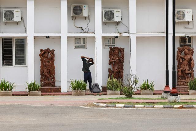 A man speaks on a mobile phone as he stands next to traditional scupltures placed below air conditioning units, at the Khurda railway station in Bhubaneswar on May 5, 2026. (Photo by Niharika KULKARNI / AFP)