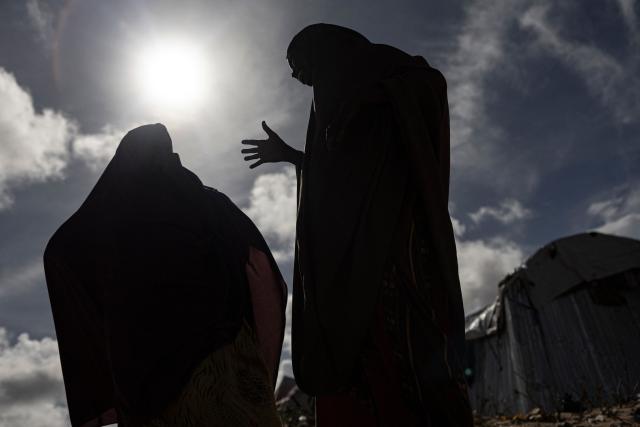 Two Somali internally displaced women stand near their makeshift shelters in a internally displaced persons (IDP) camp in Ceel Cad, Kismayo town, on April 20, 2026. Millions of people in Somalia are facing the repercussions of a severe drought after three consecutive failed raining seasons.  Kismayo, the capital of Jubaland State in southern Somalia, is one of the largest IDP-receiving cities in the Horn of Africa country, receiving hundreds of thousands of people fleeing the prolonged drought and conflict. (Photo by SIMON MAINA / AFP)
