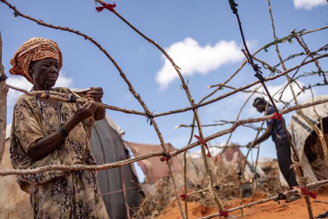 A newly arrived Somali woman build her family hut in an internally displaced persons (IDP) camp in the outskirts of Kismayo town, on April 21, 2026. Millions of people in Somalia are facing the repercussions of a severe drought after three consecutive failed raining seasons. Kismayo, the capital of Jubaland State in southern Somalia, is one of the largest IDP-receiving cities in the Horn of Africa country, receiving hundreds of thousands of people fleeing the prolonged drought and conflict. Save the Children provides health and nutrition services across the camp. (Photo by SIMON MAINA / AFP)