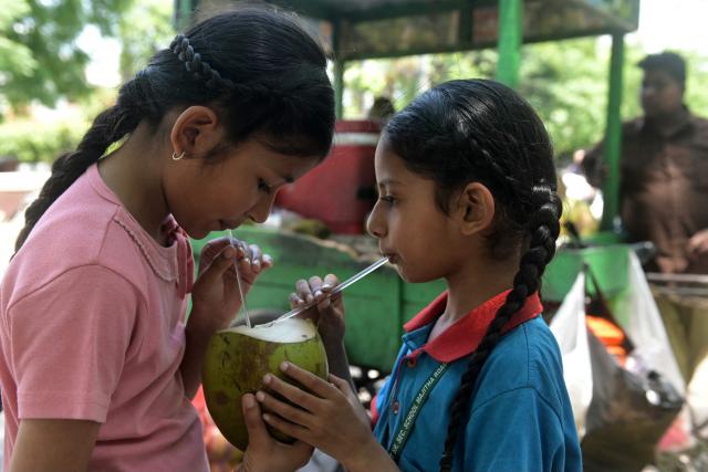 Children drink coconut water on a hot summer day along a street in Amritsar on May 5, 2026. (Photo by Narinder NANU / AFP)