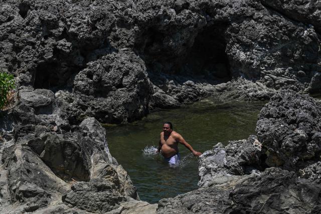 A man takes a dip in the sea by a rocky coastline in Santa, Ilocos Sur on May 5, 2026. (Photo by JAM STA ROSA / AFP)