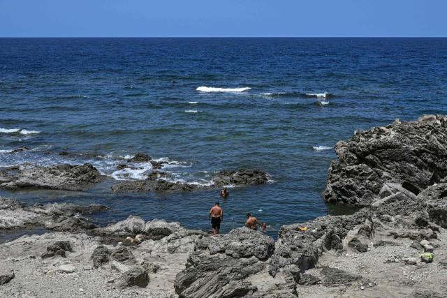 Men take a dip in the sea by a rocky coastline in Santa, Ilocos Sur on May 5, 2026. (Photo by Jam STA ROSA / AFP)
