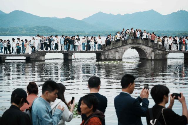 People crowd a walkway and bridge over West Lake in Hangzhou, in China’s eastern Zhejiang province on May 3, 2026, during a five-day national May Day holiday. (Photo by CN-STR / AFP) / China OUT