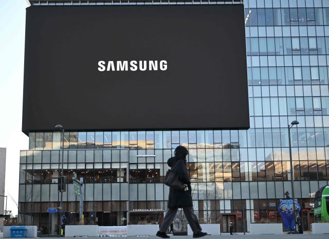 (FILES) A woman walks past a large electronic screen showing the logo of Samsung Electronics at Gwanghwamun square in central Seoul on January 8, 2026. The market value of Samsung Electronics topped $1 trillion for the first time on May 6, 2026, riding an AI chip boom that has sent South Korean stocks to record highs. (Photo by Jung Yeon-je / AFP)
