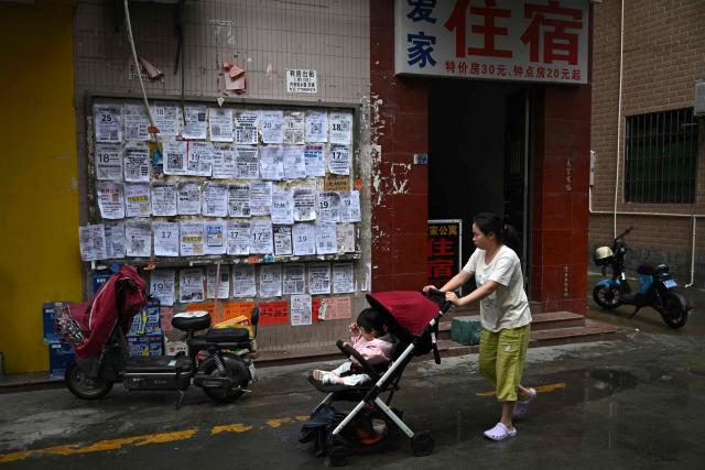 This picture taken on April 28, 2026 shows a woman pushing a stroller with a baby next to job advertisements displayed on a board in Foshan, in southern China's Guangdong province. Vacuum cleaners and vapes could get more expensive if the Iran war drags on for much longer, Chinese factory owners and traders warn, as the world's manufacturing hub reels from "crazy" costs. (Photo by Pedro PARDO / AFP) / To go with 'CHINA-IRAN-MANUFACTURING-TRADE-PLASTIC,FOCUS' by Mary YANG and Tommy WANG