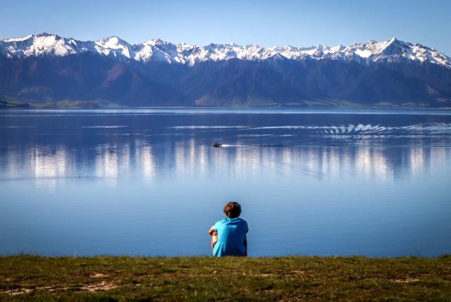(FILES) In this photo taken on October 19, 2023, a boy watches a boat on Lake Hawea, located near Queenstown on the South Island of New Zealand. New Zealand, which attracts millions of tourists each year with its pristine nature and spectacular landscapes, is facing a legal challenge over "magical thinking" in its climate promises. The country's goal, enshrined in law, is to have net-zero greenhouse gas emissions by 2050, excluding methane produced by waste and agriculture. (Photo by DAVID GRAY / AFP) / To go with AFP story NZealand-climate-law,FOCUS by Ben Strang