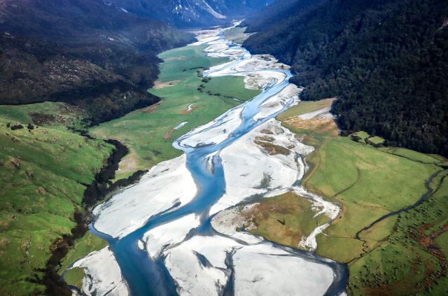 (FILES) In this photo taken on October 20, 2023, the Wilkin River flows through paddocks located near Makarora on the South Island of New Zealand. New Zealand, which attracts millions of tourists each year with its pristine nature and spectacular landscapes, is facing a legal challenge over "magical thinking" in its climate promises. The country's goal, enshrined in law, is to have net-zero greenhouse gas emissions by 2050, excluding methane produced by waste and agriculture. (Photo by DAVID GRAY / AFP) / To go with AFP story NZealand-climate-law,FOCUS by Ben Strang
