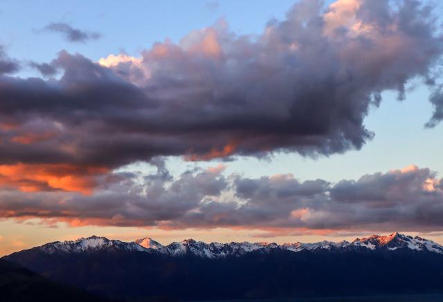 (FILES) In this photo taken on October 21, 2023, snow covers mountains at sunset above Lake Hawea, located near Queenstown on the South Island of New Zealand. New Zealand, which attracts millions of tourists each year with its pristine nature and spectacular landscapes, is facing a legal challenge over "magical thinking" in its climate promises. The country's goal, enshrined in law, is to have net-zero greenhouse gas emissions by 2050, excluding methane produced by waste and agriculture. (Photo by DAVID GRAY / AFP) / To go with AFP story NZealand-climate-law,FOCUS by Ben Strang