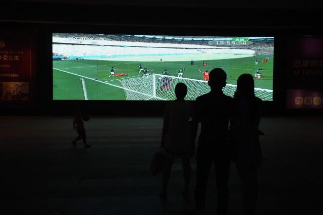 (FILES) This photo taken on June 30, 2014 shows people watching a TV screen showing a 2014 football World Cup replay, outside a shopping mall in Beijing. Swathes of football-mad Asia from China to India, Malaysia and Thailand, are yet to announce broadcast rights for the biggest-ever World Cup with kick-off barely one month away. (Photo by GREG BAKER / AFP)