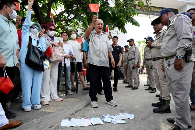 (FILES) Chinese nationals believed to be Huione Pay creditors hold Chinese national flags in front of security personnel during a protest near the National Bank of Cambodia (NBC) headquarters in Phnom Penh on April 27, 2026. A cousin of Cambodian Prime Minister Hun Manet said May 6 he owned a 30 percent stake in a digital payments platform linked to cyberscams and money laundering and sanctioned by Washington. (Photo by TANG CHHIN Sothy / AFP)