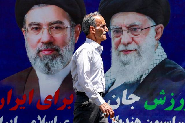 A man walks past a large banner depicting Iran's current supreme leader Ayatollah Mojtaba Khamenei and his predecessor and late father Ali Khamenei along a street in Tehran on May 6, 2026. The United States and Pakistan, a key mediator in the Middle East war, expressed new hope of talks leading to a peace deal with Iran on May 6, after President Donald Trump halted a plan to guide ships through the Strait of Hormuz. (Photo by AFP) / 
