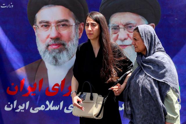 Women walk past a large banner depicting Iran's current supreme leader Ayatollah Mojtaba Khamenei and his predecessor and late father Ali Khamenei along a street in Tehran on May 6, 2026. The United States and Pakistan, a key mediator in the Middle East war, expressed new hope of talks leading to a peace deal with Iran on May 6, after President Donald Trump halted a plan to guide ships through the Strait of Hormuz. (Photo by AFP) / 