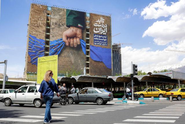 A woman crosses a street near a billboard on the facade of a building depicting the Strait of Hormuz with a caption in Persian reading "Forever in Iran’s Hand", at Vanak Square in Tehran on May 6, 2026. The United States and Pakistan, a key mediator in the Middle East war, expressed new hope of talks leading to a peace deal with Iran on May 6, after President Donald Trump halted a plan to guide ships through the Strait of Hormuz. (Photo by AFP) / 