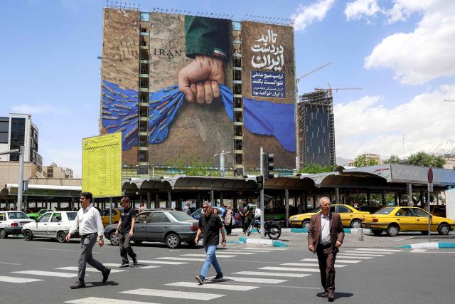 People cross a street near a billboard on the facade of a building depicting the Strait of Hormuz with a caption in Persian reading "Forever in Iran’s Hand", at Vanak Square in Tehran on May 6, 2026. The United States and Pakistan, a key mediator in the Middle East war, expressed new hope of talks leading to a peace deal with Iran on May 6, after President Donald Trump halted a plan to guide ships through the Strait of Hormuz. (Photo by AFP) / 