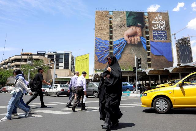 A woman crosses a street near a billboard on the facade of a building depicting the Strait of Hormuz with a caption in Persian reading "Forever in Iran’s Hand", at Vanak Square in Tehran on May 6, 2026. The United States and Pakistan, a key mediator in the Middle East war, expressed new hope of talks leading to a peace deal with Iran on May 6, after President Donald Trump halted a plan to guide ships through the Strait of Hormuz. (Photo by AFP) / 