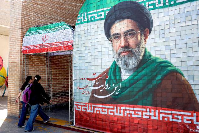 Women walk past a banner depicting Iran's current supreme leader Ayatollah Mojtaba Khamenei along a street Tehran on May 6, 2026. The United States and Pakistan, a key mediator in the Middle East war, expressed new hope of talks leading to a peace deal with Iran on May 6, after President Donald Trump halted a plan to guide ships through the Strait of Hormuz. (Photo by AFP) / 