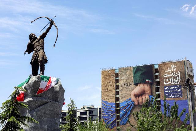 A statue depicting Persian mythical figure Arash the Archer, who according to tradition defined the border area between Persia and the Turanians, is displayed near a billboard on the facade of a building depicting the Strait of Hormuz with a caption in Persian reading "Forever in Irans Hand", at Vanak Square in Tehran on May 6, 2026. The United States and Pakistan, a key mediator in the Middle East war, expressed new hope of talks leading to a peace deal with Iran on May 6, after President Donald Trump halted a plan to guide ships through the Strait of Hormuz. (Photo by AFP) / 