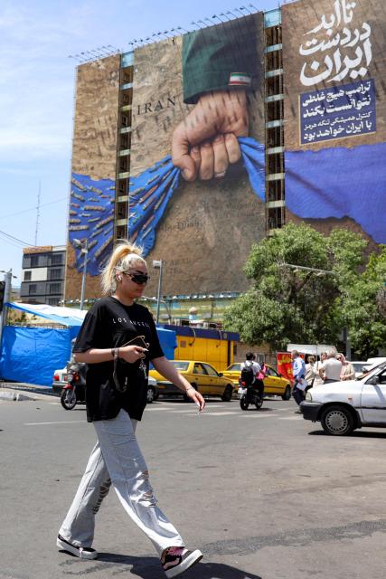 A woman crosses a street near a billboard on the facade of a building depicting the Strait of Hormuz with a caption in Persian reading "Forever in Iran’s Hand", at Vanak Square in Tehran on May 6, 2026. The United States and Pakistan, a key mediator in the Middle East war, expressed new hope of talks leading to a peace deal with Iran on May 6, after President Donald Trump halted a plan to guide ships through the Strait of Hormuz. (Photo by AFP) / 