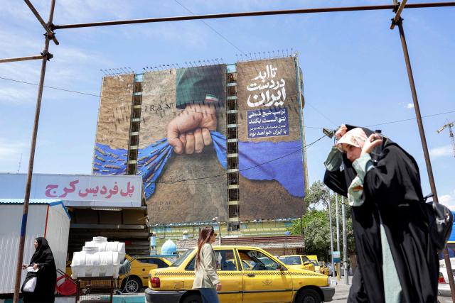 A woman adjusts her headdress as she walks near a billboard on the facade of a building depicting the Strait of Hormuz with a caption in Persian reading "Forever in Iran’s Hand", at Vanak Square in Tehran on May 6, 2026. The United States and Pakistan, a key mediator in the Middle East war, expressed new hope of talks leading to a peace deal with Iran on May 6, after President Donald Trump halted a plan to guide ships through the Strait of Hormuz. (Photo by AFP) / 