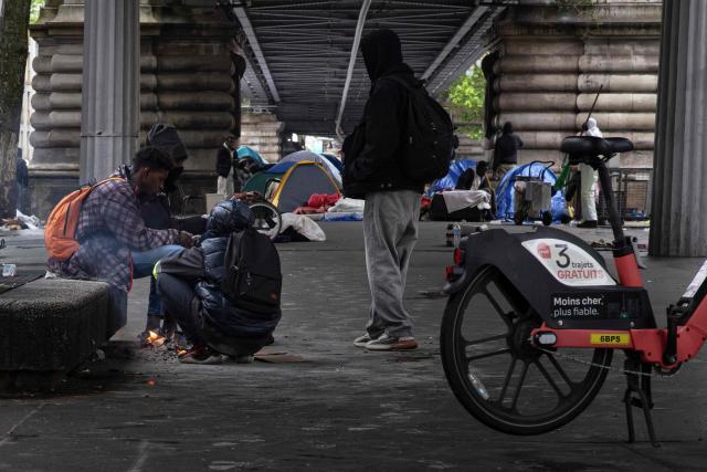 Migrants warm themselves around a fire next to their tents under the elevated Stalingrad metro station in Paris on May 6, 2026. (Photo by JOEL SAGET / AFP)