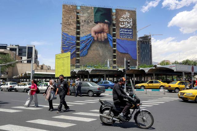 A motorist rides a scooter along a street near a billboard on the facade of a building depicting the Strait of Hormuz with a caption in Persian reading "Forever in Iran’s Hand", at Vanak Square in Tehran on May 6, 2026. The United States and Pakistan, a key mediator in the Middle East war, expressed new hope of talks leading to a peace deal with Iran on May 6, after President Donald Trump halted a plan to guide ships through the Strait of Hormuz. (Photo by AFP) / 