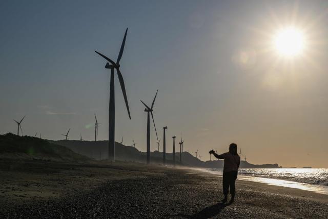 A woman films next to wind turbines along the shore in Bangui in the northern Philippines province of Ilocos Norte on May 6, 2026. (Photo by Jam STA ROSA / AFP)