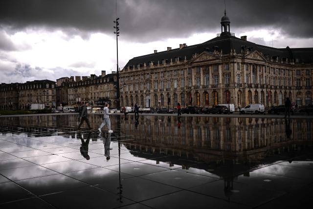 Passers-by walk across the Miroir d'Eau as dark clouds loom over on a rainy day in Bordeaux, south-western France, on May 6, 2026. (Photo by Christophe ARCHAMBAULT / AFP)