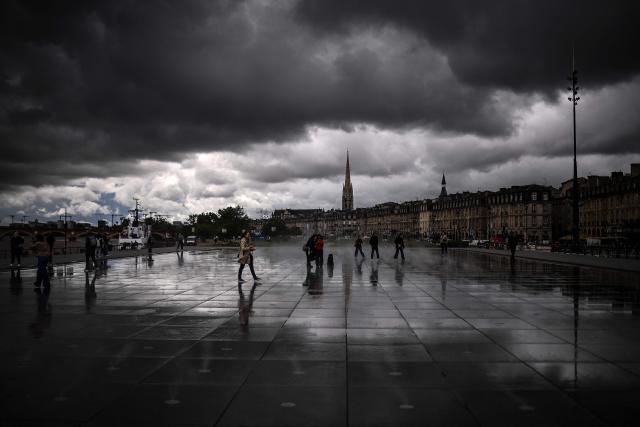 TOPSHOT - Passers-by walk across the Miroir d'Eau as dark clouds loom over on a rainy day in Bordeaux, south-western France, on May 6, 2026. (Photo by Christophe ARCHAMBAULT / AFP)