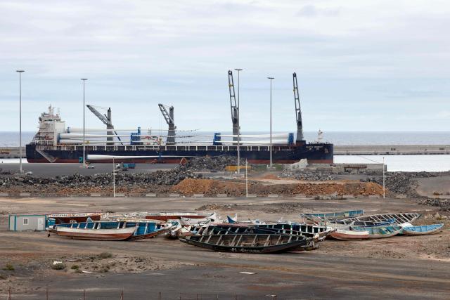 A large cargo ship is seen behind migrant boats stacked at the port of Granadilla de Abona, on the island of Tenerife in Spain's Canary Islands archipielago, on May 6, 2026. A cruise ship hit by a hantavirus outbreak will dock "within three days" at Granadilla on the island of Tenerife, Spains health minister said today, despite opposition from the Canary Islands regional government. "A joint system for health assessment and evacuation will be put in place to repatriate all passengers, unless their medical condition prevents it," the health minister told during a news conference. (Photo by Oscar DEL POZO / AFP)