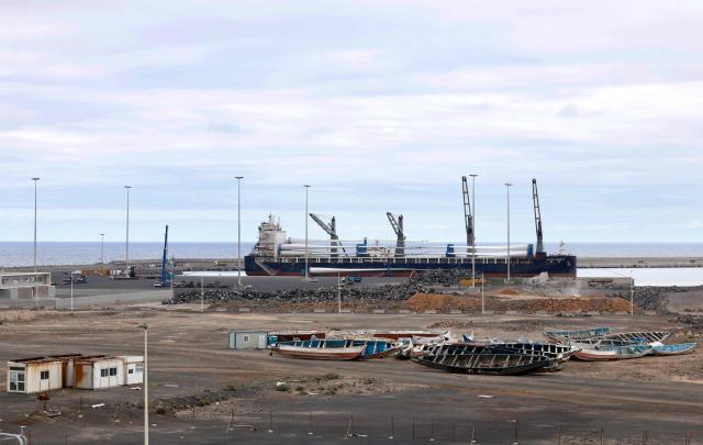 A large cargo ship is seen behind migrant boats stacked at the port of Granadilla de Abona, on the island of Tenerife in Spain's Canary Islands archipielago, on May 6, 2026. A cruise ship hit by a hantavirus outbreak will dock "within three days" at Granadilla on the island of Tenerife, Spains health minister said today, despite opposition from the Canary Islands regional government. "A joint system for health assessment and evacuation will be put in place to repatriate all passengers, unless their medical condition prevents it," the health minister told during a news conference. (Photo by Oscar DEL POZO / AFP)