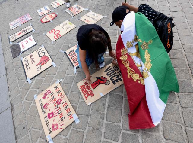 Supporters of the son of Iran's last shah, exiled Crown Prince Reza Pahlavi, one drapped with an Iranian pre-Islamic revolution of 1979 flag, prepare placards during a small protest outside of Austrian parliament in Vienna on May 6, 2026. (Photo by Joe Klamar / AFP)