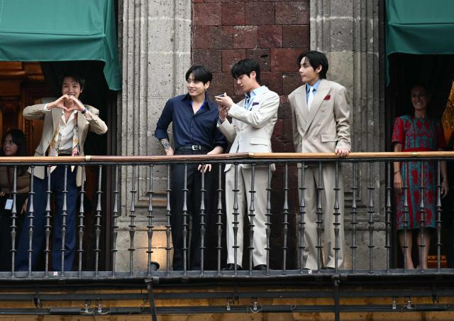 South Korean K-pop band BTS members gesture to fans form the balcony of the National Palace as Mexico's President Claudia Sheinbaum (R) looks on at Zocalo square in Mexico City on May 6, 2026. BTS will hold three sold-out shows at Estadio GNP Seguros in Mexico city on May 7, 9, and 10. (Photo by YURI CORTEZ / AFP)
