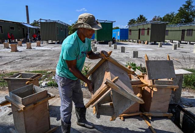 A worker carries wooden formwork near housing units made from shipping containers in Havana on May 7, 2026. Amid a housing deficit exceeding 800,000 homes, Cuba has begun converting shipping containers into housing units. Initially intended to transport equipment for solar parks, these metal modules are now being adapted as homes for vulnerable groups, including families affected by climate events, recipients of state subsidies and young people without family support. (Photo by YAMIL LAGE / AFP)