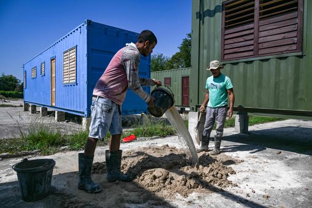 Workers mix cement beside housing units made from shipping containers in Havana on May 7, 2026. Amid a housing deficit exceeding 800,000 homes, Cuba has begun converting shipping containers into housing units. Initially intended to transport equipment for solar parks, these metal modules are now being adapted as homes for vulnerable groups, including families affected by climate events, recipients of state subsidies and young people without family support. (Photo by YAMIL LAGE / AFP)