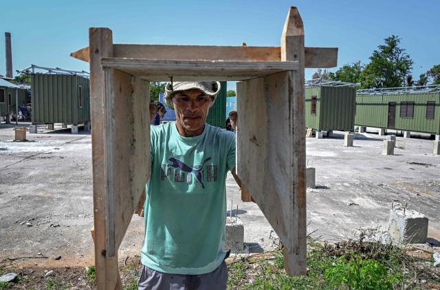 A worker carries wooden formwork near housing units made from shipping containers in Havana on May 7, 2026. Amid a housing deficit exceeding 800,000 homes, Cuba has begun converting shipping containers into housing units. Initially intended to transport equipment for solar parks, these metal modules are now being adapted as homes for vulnerable groups, including families affected by climate events, recipients of state subsidies and young people without family support. (Photo by YAMIL LAGE / AFP)