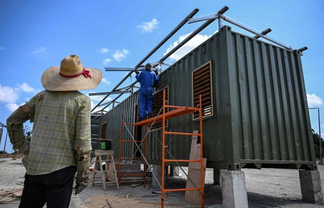 Workers assemble a metal structure on top of a housing unit made from a shipping container in Havana on May 7, 2026. Amid a housing deficit exceeding 800,000 homes, Cuba has begun converting shipping containers into housing units. Initially intended to transport equipment for solar parks, these metal modules are now being adapted as homes for vulnerable groups, including families affected by climate events, recipients of state subsidies and young people without family support. (Photo by YAMIL LAGE / AFP)